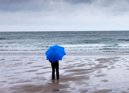 Person holding umbrella looking at stormy sea